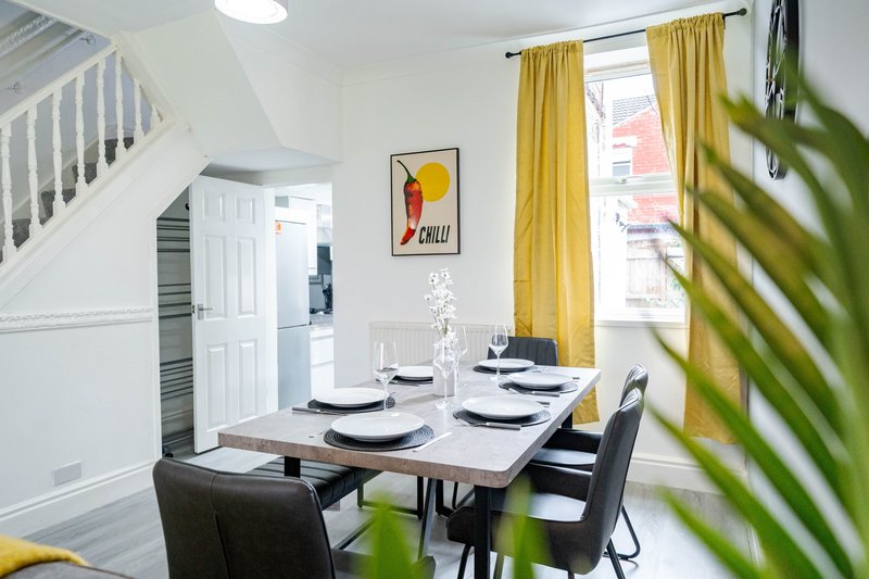 Bright dining room with white table, black chairs, yellow curtains and staircase visible