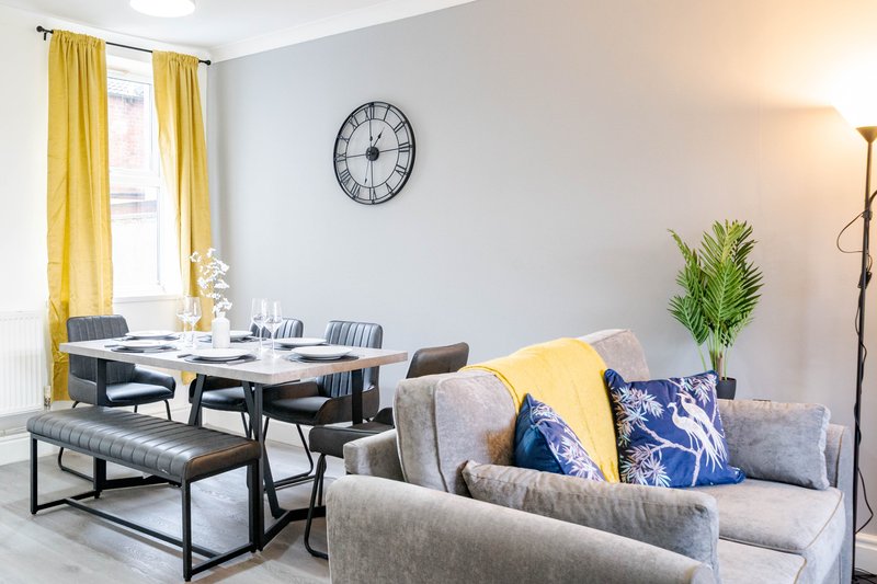 Open-plan living and dining area with grey sofa, dining table, yellow curtains and wall clock