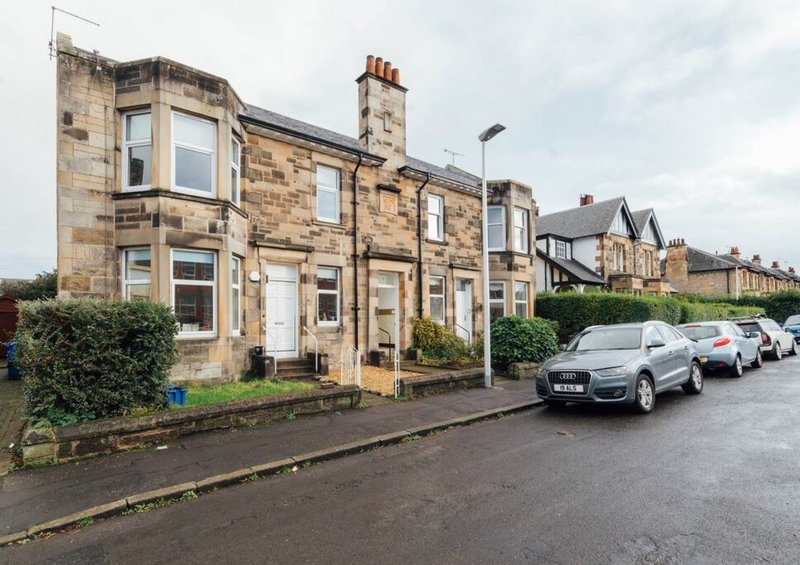Stone terrace houses with parked cars on street and front gardens visible