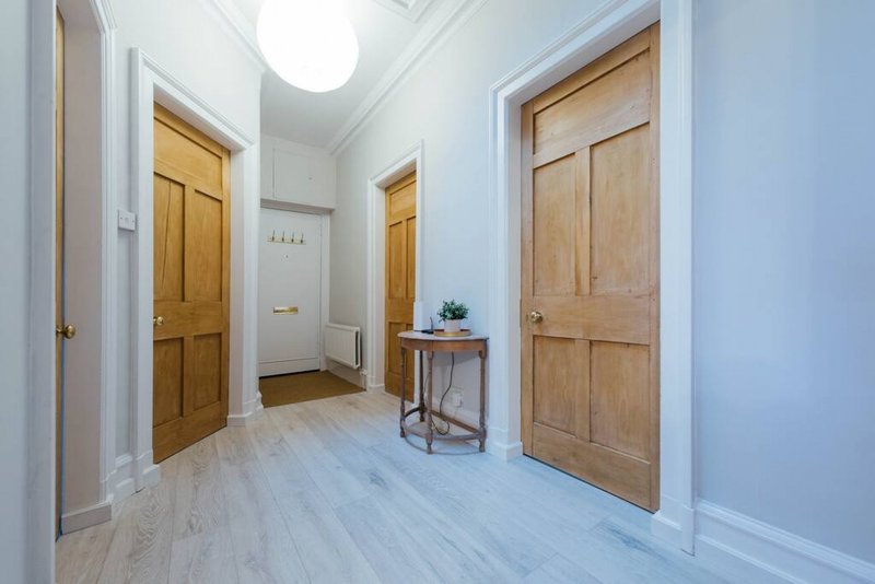 Bright hallway with wooden doors, light flooring, white walls and small side table