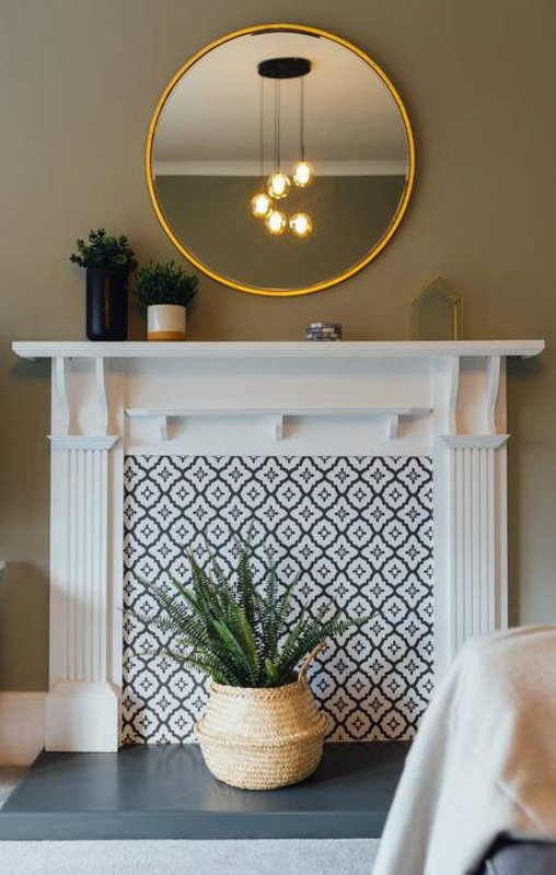Modern fireplace mantel with gold-framed mirror, pendant lights, potted plant and decorative objects