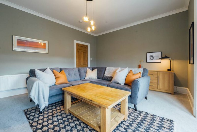 Modern living room with blue sofa, wooden coffee table, pendant lights and neutral walls
