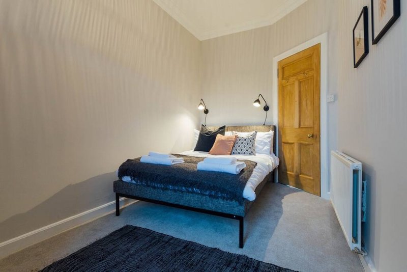 Bedroom with double bed, blue bedding, wooden door, wall sconces and rug