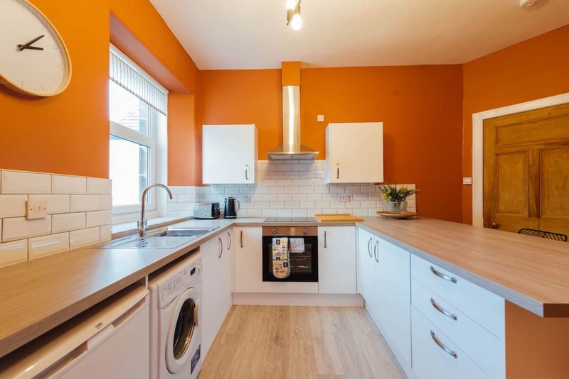 Modern kitchen with orange walls, white cabinetry, wooden worktops and integrated appliances