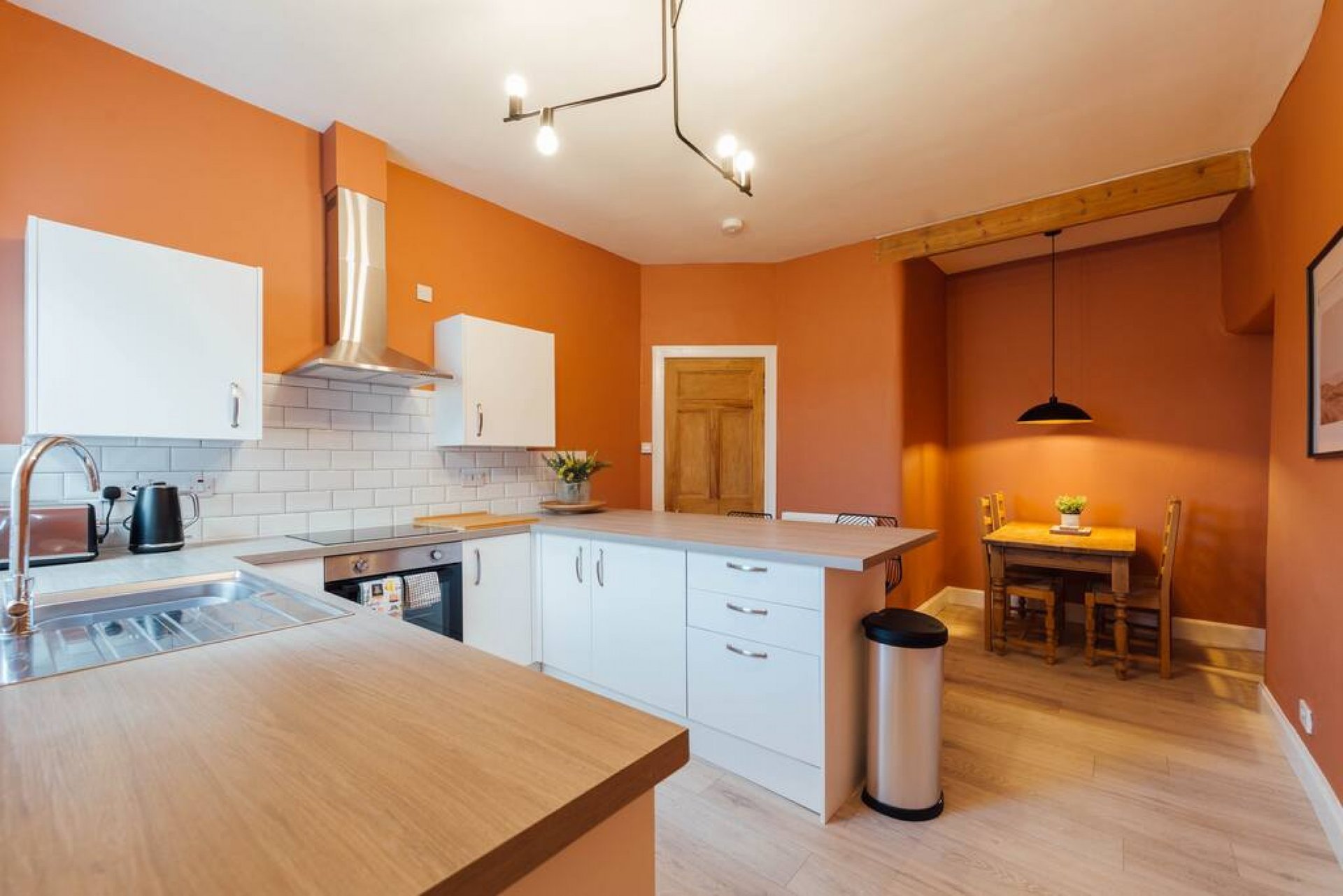 Modern kitchen with orange walls, white cabinetry, wooden worktops and open-plan dining area