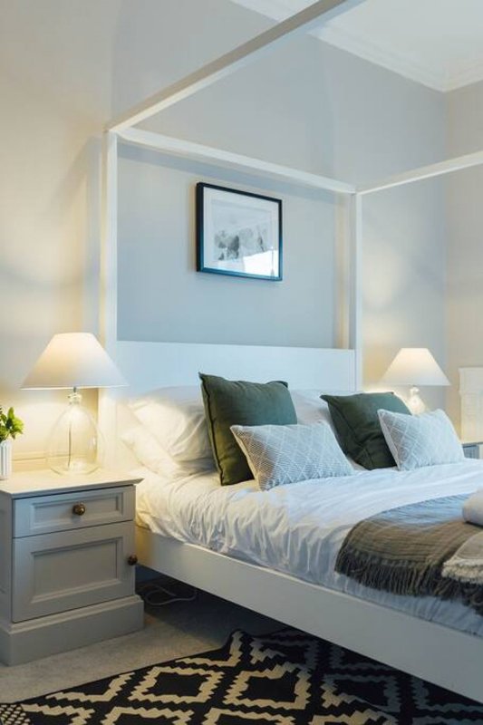 Modern bedroom with four-poster bed, decorative pillows, bedside tables with lamps, and framed wall art