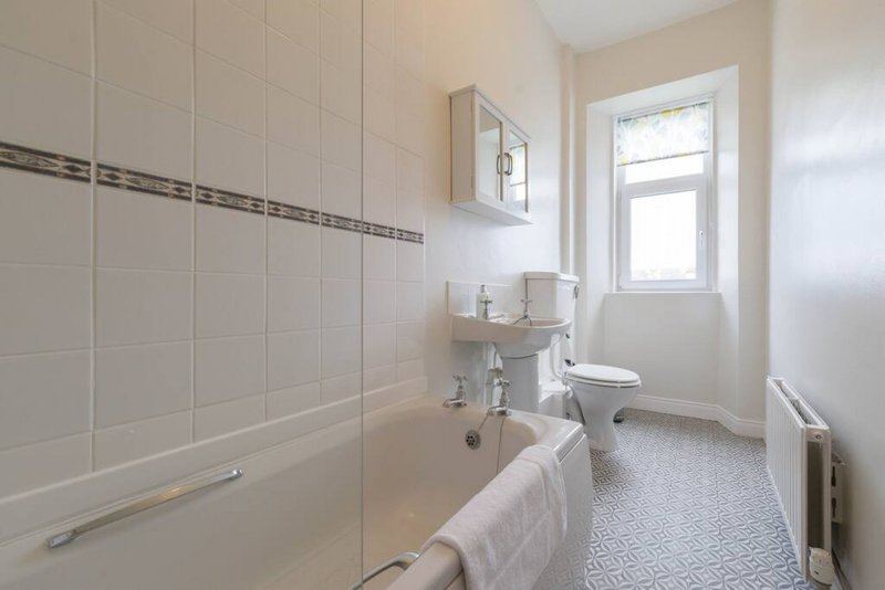 Clean bathroom with bathtub, shower screen, sink, toilet and window