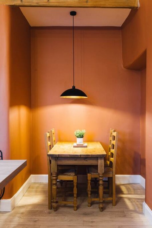Warm orange dining alcove with wooden table, chairs, pendant light and potted plant