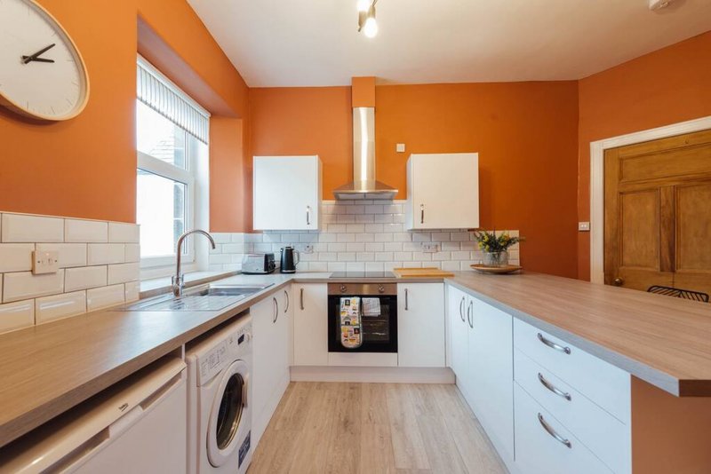 Modern kitchen with orange walls, white cabinetry, wooden countertops and subway tile backsplash