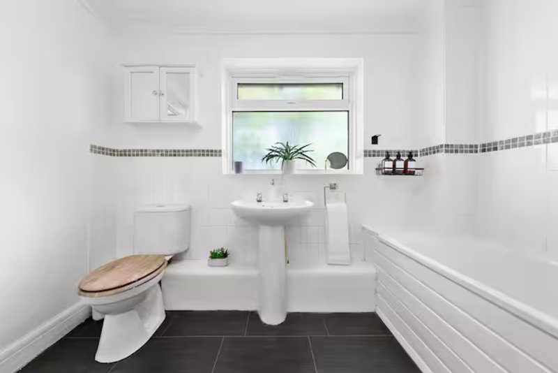 Clean modern bathroom with toilet, pedestal sink, window and dark tile flooring