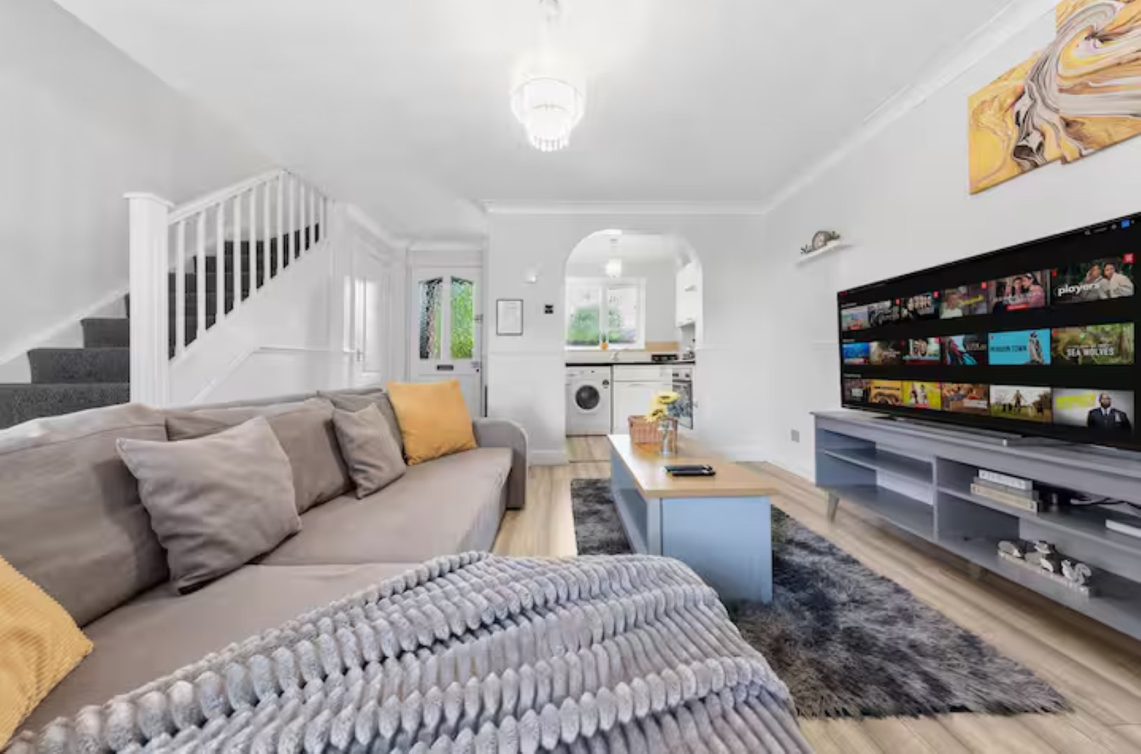 Open-plan living room with sofa, bed, stairs, shelving unit and kitchen visible
