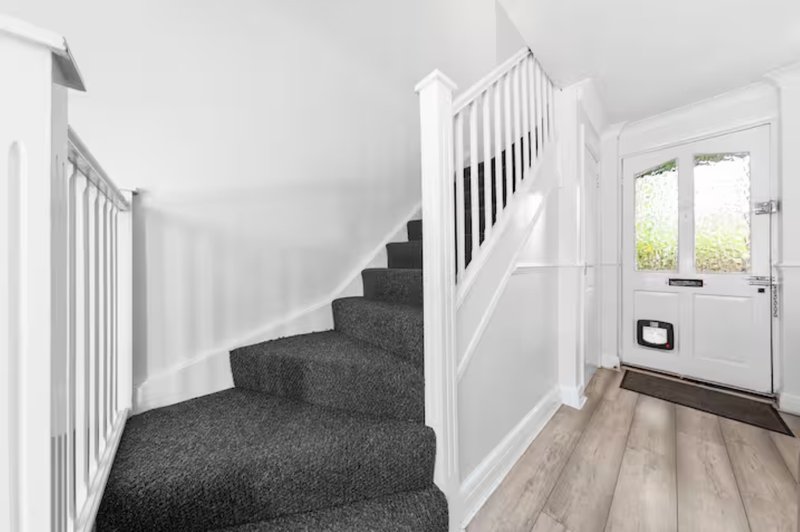 Bright hallway with staircase, white railings, grey carpeted steps and wooden flooring