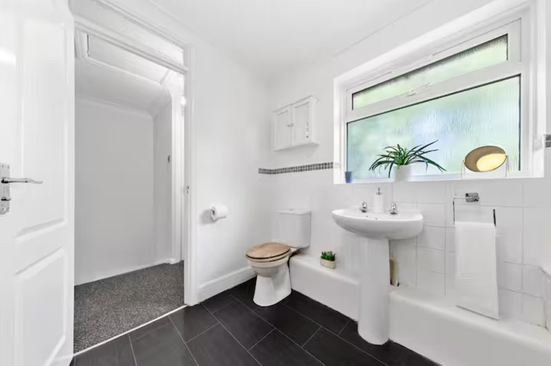 Bathroom with white suite, pedestal sink, toilet, bathtub, dark floor tiles and window