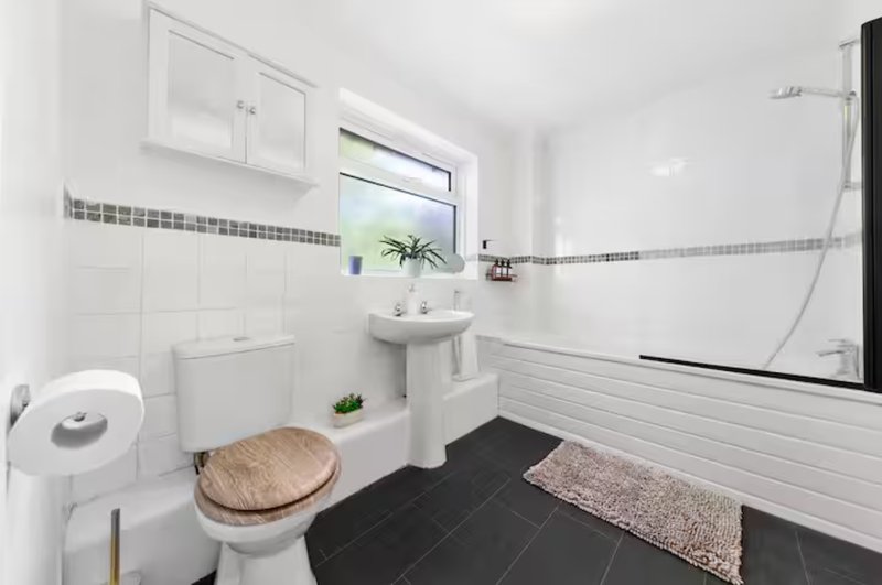 Modern bathroom with white tiles, black floor, toilet, pedestal sink and shower enclosure