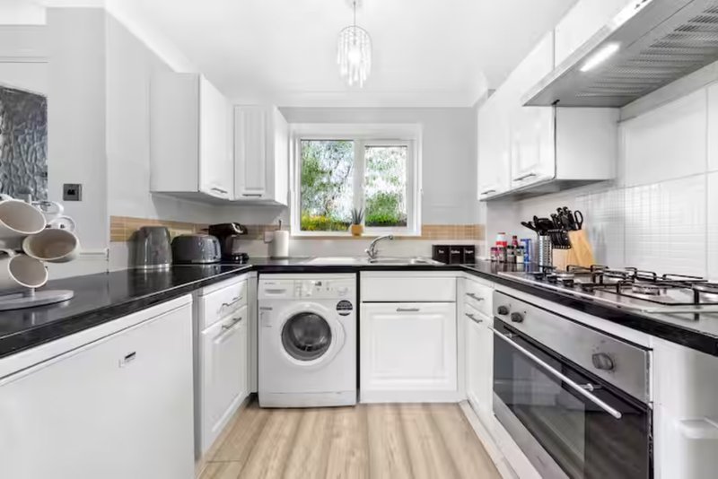 Modern kitchen with white cabinets, black countertops, stainless steel appliances and natural light