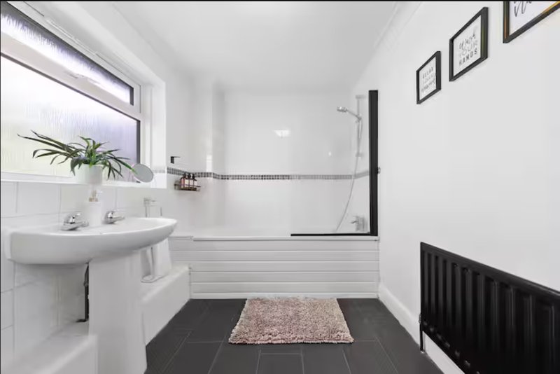 Modern white bathroom with pedestal sink, black and white tile, shower enclosure and plant