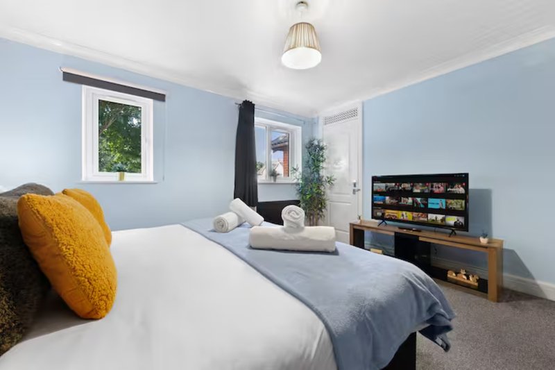 Modern bedroom with double bed, yellow cushion, blue walls and wooden TV unit