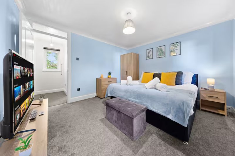 Bright bedroom with double bed, colorful cushions, wooden furniture and light blue walls