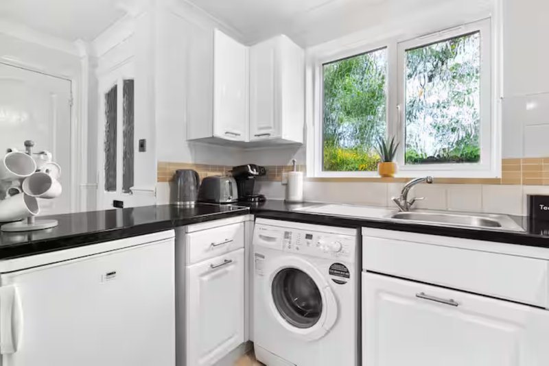 Modern kitchen with white cabinetry, black countertops, integrated appliances and garden view
