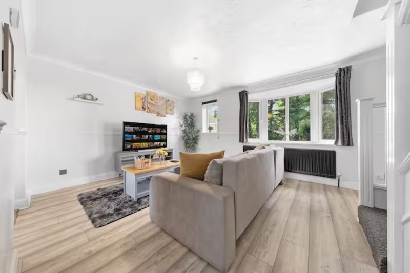 Bright living room with grey sofa, wooden flooring, TV unit, and large windows overlooking garden
