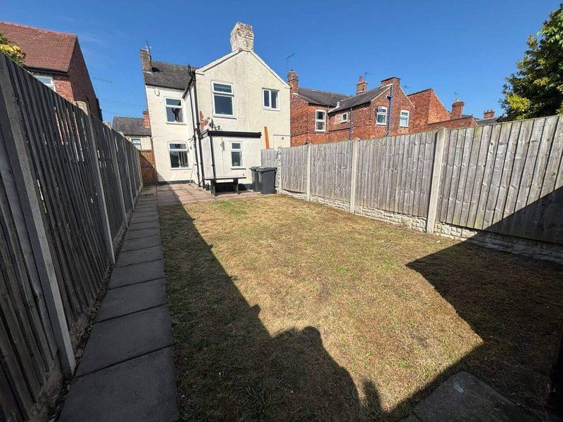 Rear garden view of cream-coloured house with grey fencing and paved pathway