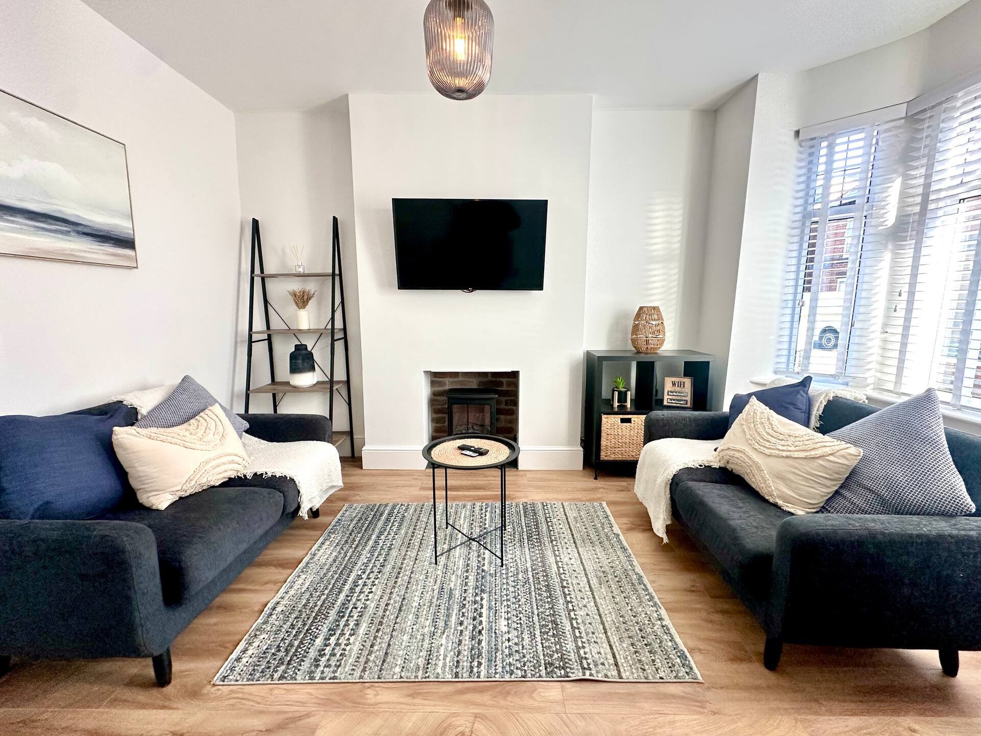 Spacious living room with two blue sofas, fireplace, wall-mounted TV, and wooden flooring