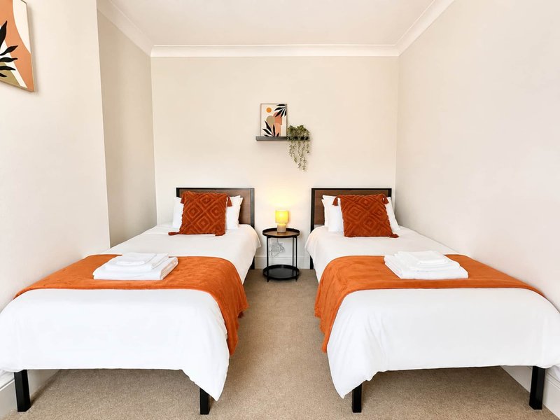 Twin bedroom with two single beds, orange bedding, white sheets, central nightstand and wall art