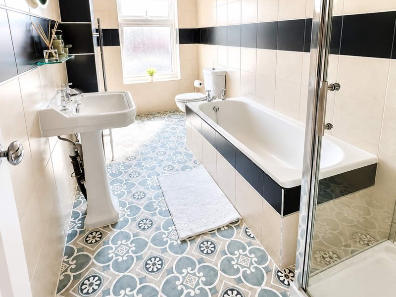 Bathroom with pedestal sink, bathtub, shower enclosure, and patterned floor tiles