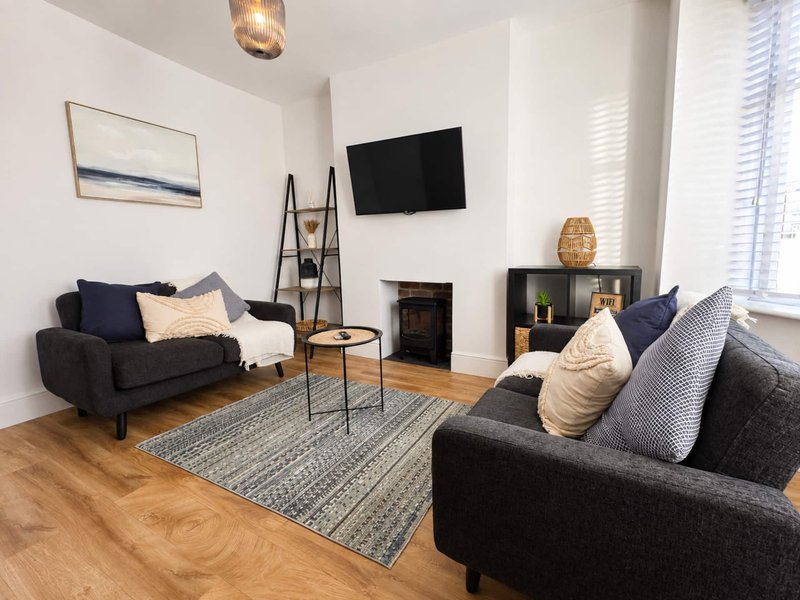 Modern living room with two dark sofas, fireplace, wall-mounted TV, and wooden flooring