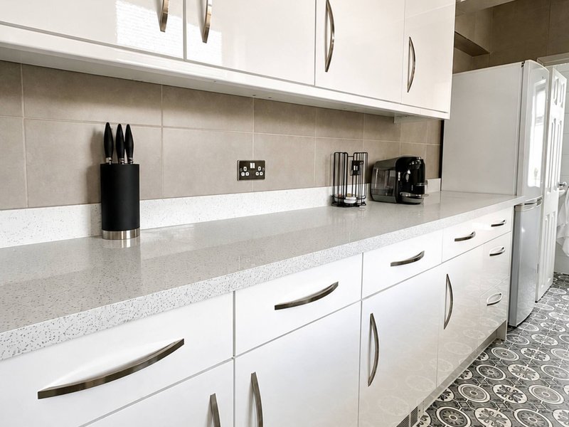 Modern white kitchen with quartz countertop, black appliances and beige tile backsplash