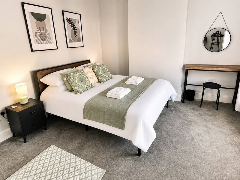Modern bedroom with double bed, green bedding, framed wall art, and grey carpet flooring