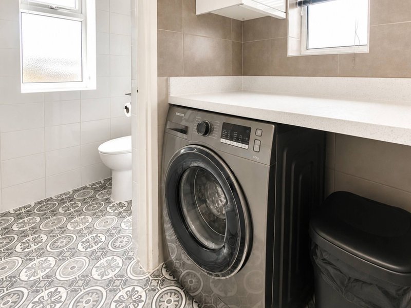 Bathroom with toilet, washing machine, white countertop and patterned floor tiles