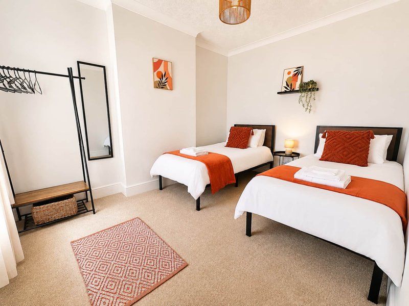 Bright bedroom with two single beds, orange bedding, carpet flooring and pendant light