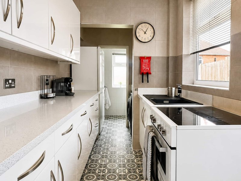 Galley kitchen with white cabinetry, beige tile walls, black countertops and appliances