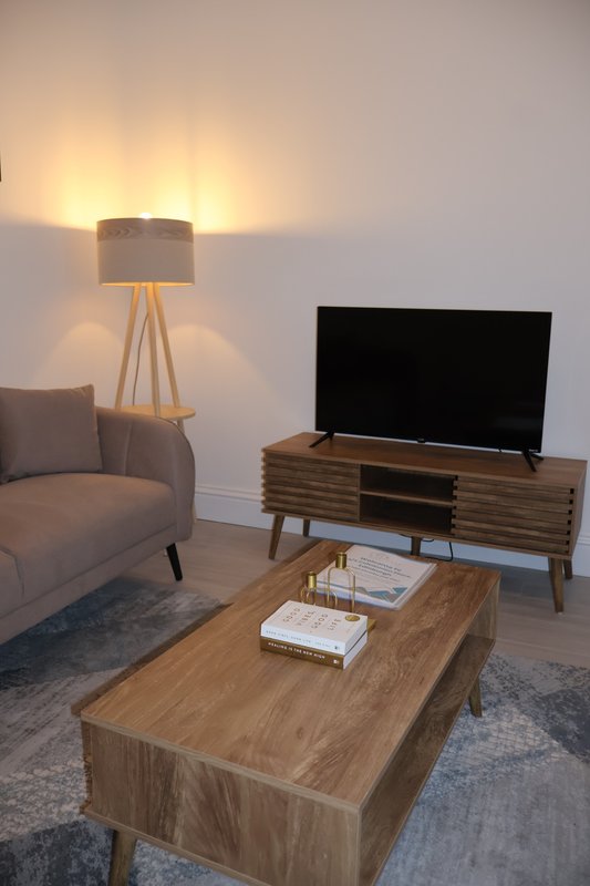 Modern living room with wooden furniture, armchair, tripod lamp, and TV stand