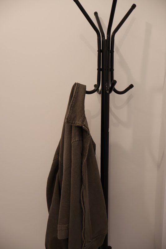 Black coat stand with brown jacket hanging on hooks against white wall