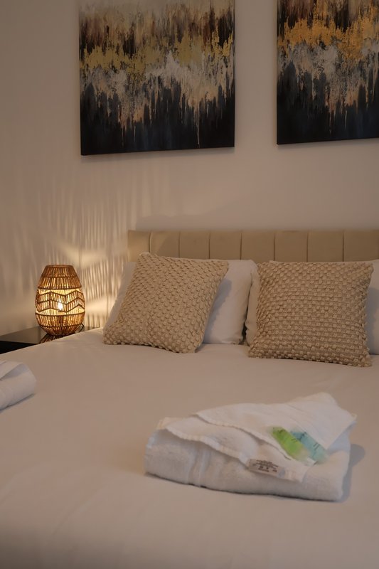 Bedroom with upholstered headboard, decorative cushions, woven bedside lamp and framed wall art