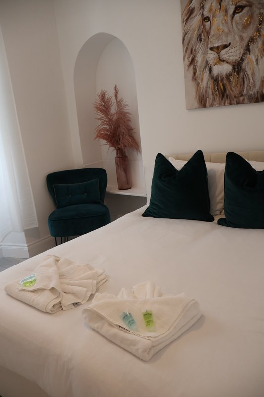 Bedroom with white bed, black cushions, dark chair, mirror, and lion wall art