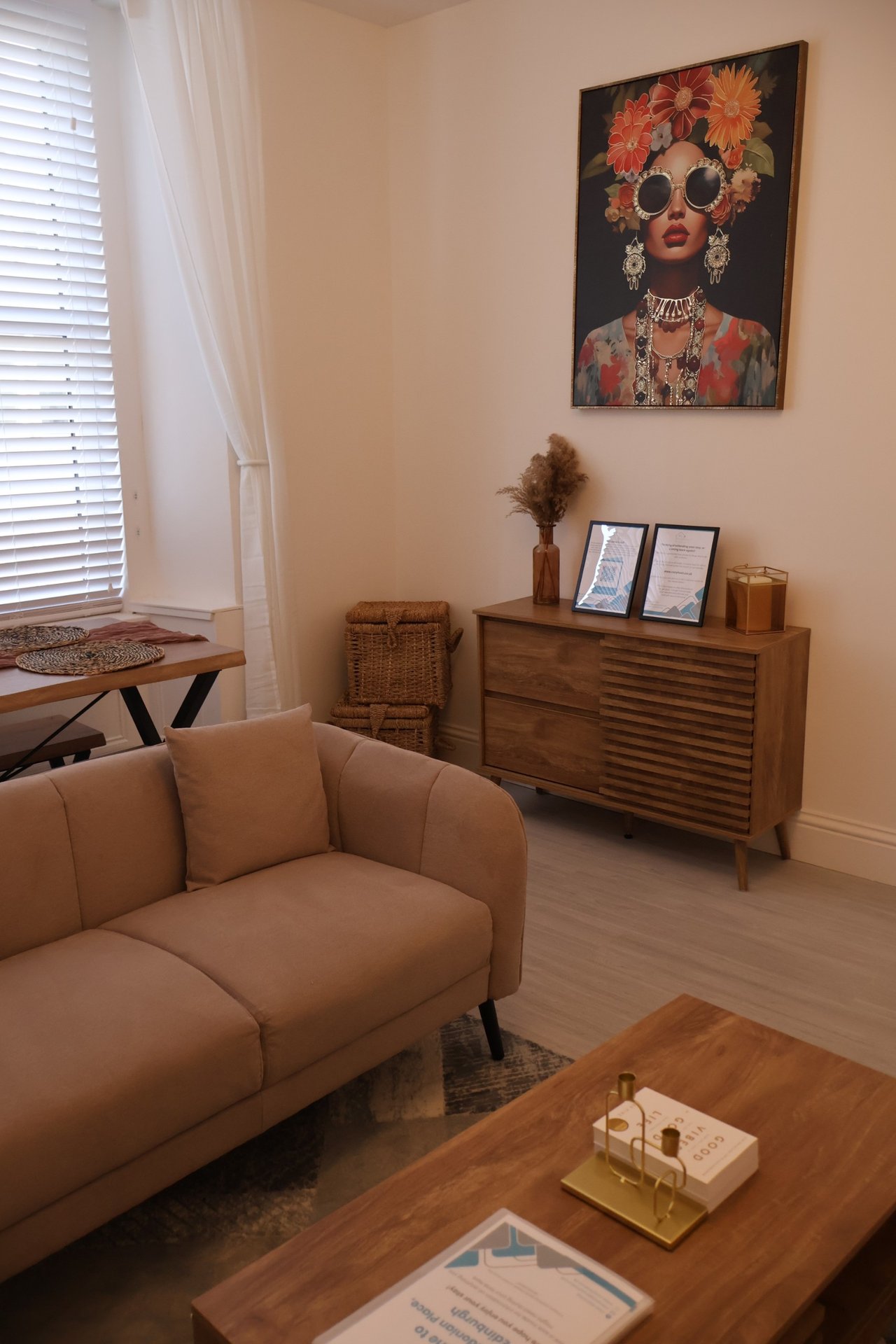 Living room with tan curved sofa, wooden dresser, wall art, and natural light from window