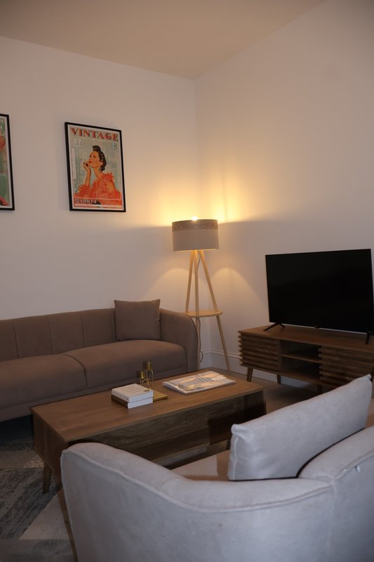 Living room with grey sofa, white armchair, wooden coffee table, tripod lamp and wall art