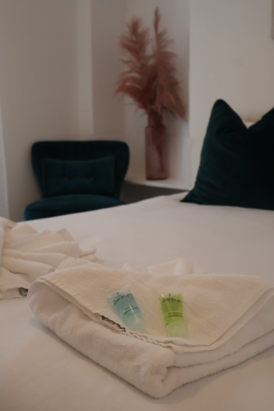 Bedroom with folded white towels, toiletries, dark chair, and decorative dried flowers