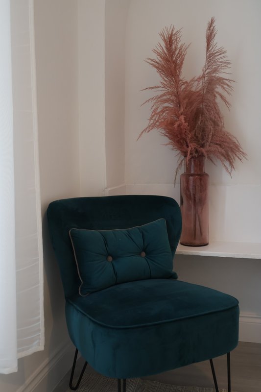 Blue velvet accent chair with cushion next to vase of dried pampas grass