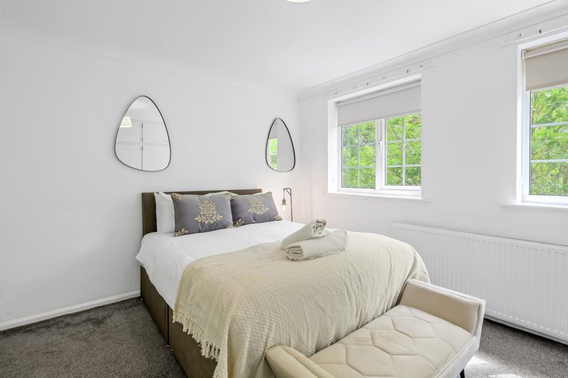 Bright bedroom with double bed, cream bedding, decorative mirrors, and large windows overlooking garden