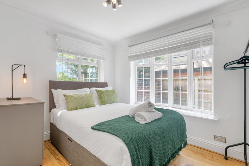 Bright bedroom with double bed, green blanket, white pillows, wooden floor and large windows