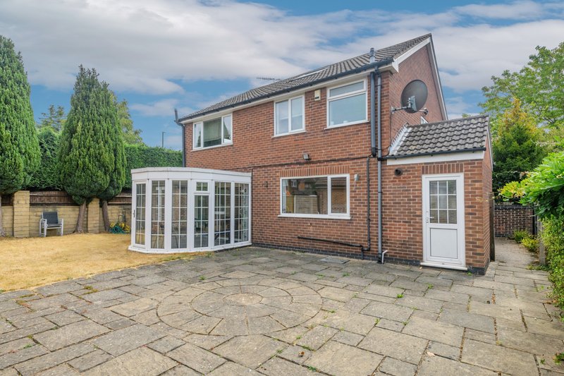 Brick suburban house with modern conservatory extension, paved patio and garden