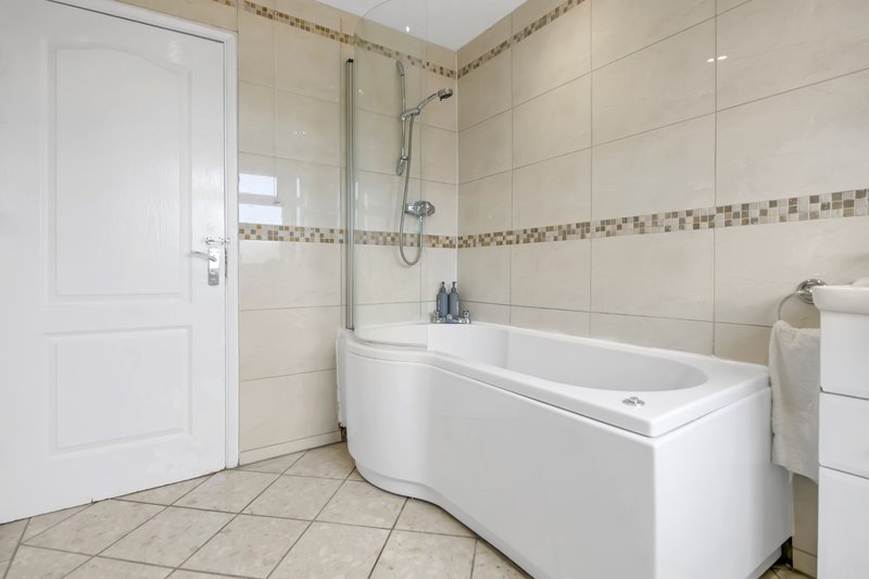 Modern bathroom with white bathtub, glass shower screen, beige tiles and white door