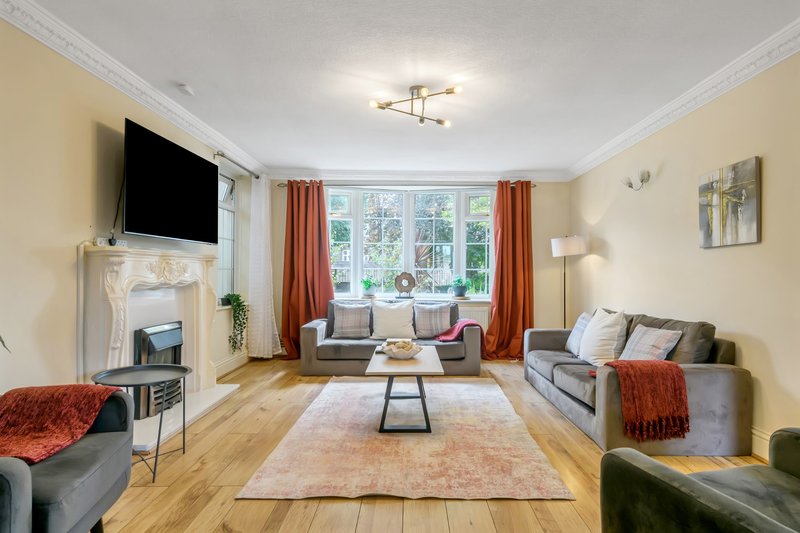 Spacious living room with fireplace, sofas, TV, large windows and wooden flooring