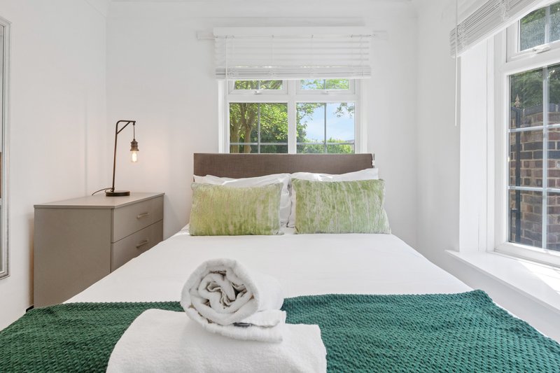 Bright bedroom with double bed, green bedding, wooden headboard and side table with lamp