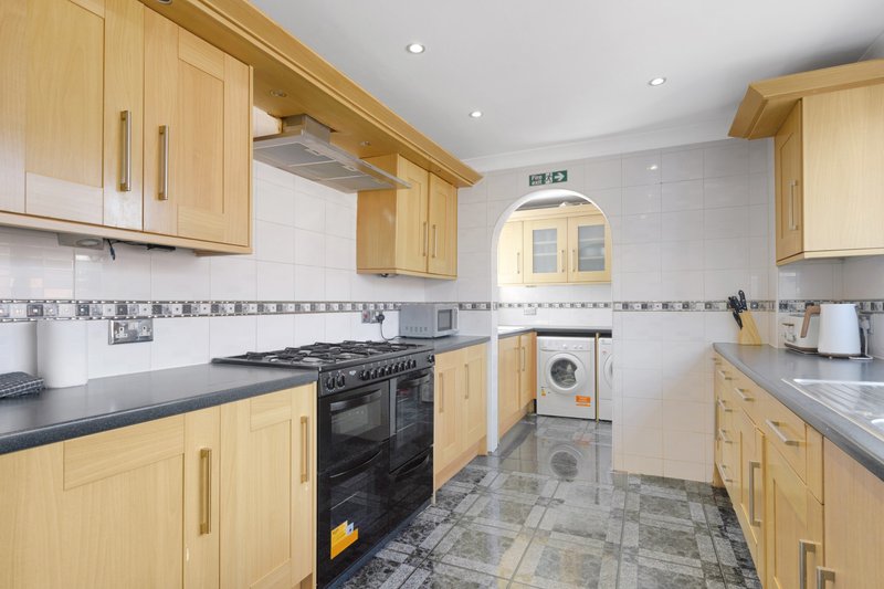 Modern kitchen with light wood cabinets, black worktops, gas range and tiled flooring