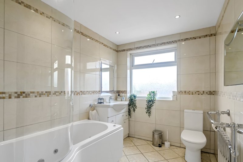 Spacious bathroom with corner bath, shower enclosure, toilet, and window with natural light